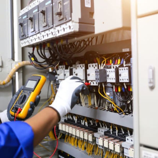 Technicien, tenant un équipement de vérification pour vérifier le câblage d'une armoire électrique industrielle